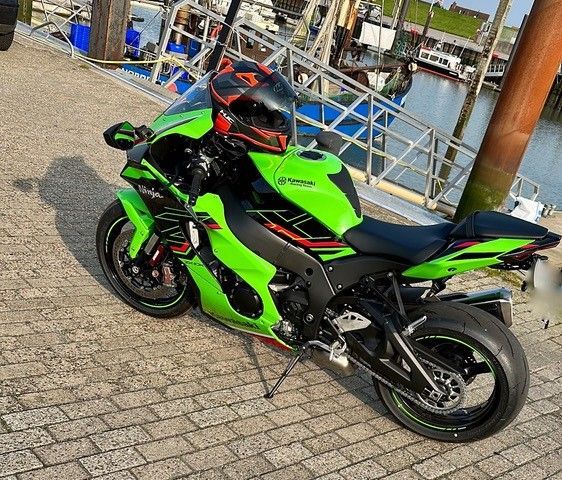 Ein grünes Motorrad ist auf einem gepflasterten Gehweg neben einem Gewässer geparkt.