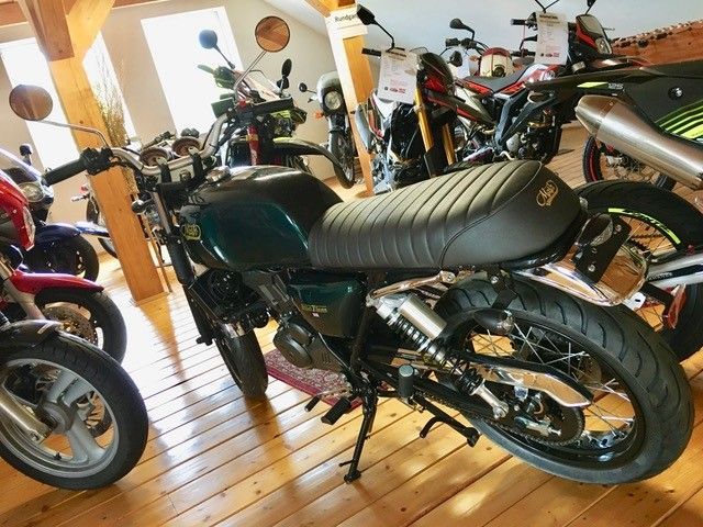 In einem Ausstellungsraum ist eine Reihe Motorräder auf einem Holzboden geparkt.