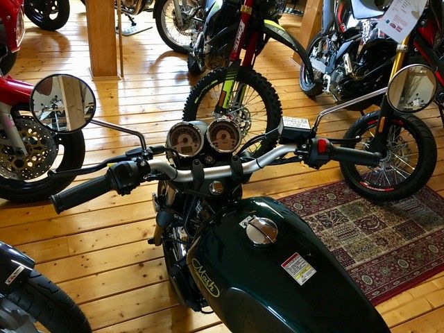 Ein grünes Motorrad steht auf einem Holzboden in einem Ausstellungsraum.