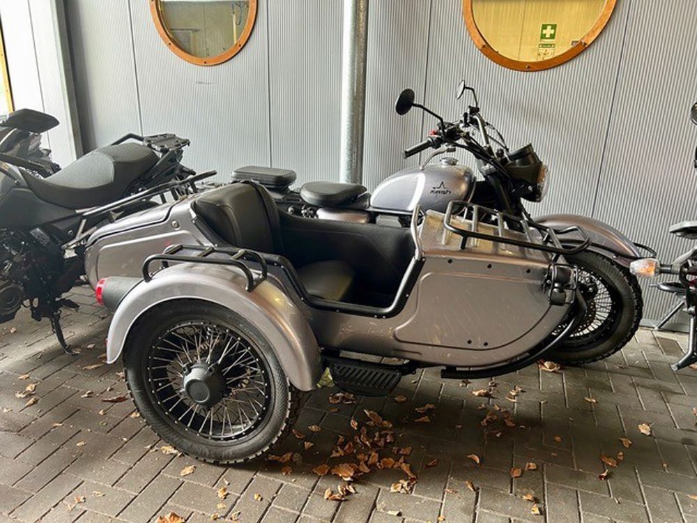 Silbernes Motorrad mit Beiwagen, das drinnen auf einem laubbedeckten Boden parkt.