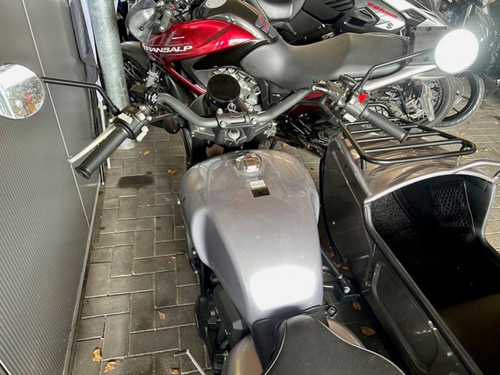 Drei geparkte Motorräder in einer schmalen Garage, darunter ein rotes, ein silbernes und ein schwarzes Motorrad.