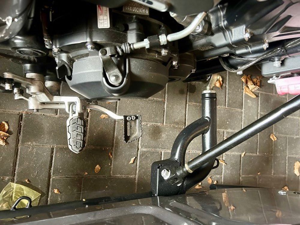Motorradmotor und Fußbedienelemente von oben betrachtet, darunter befinden sich ein schwarzer Rahmen und ein gefliester Boden.