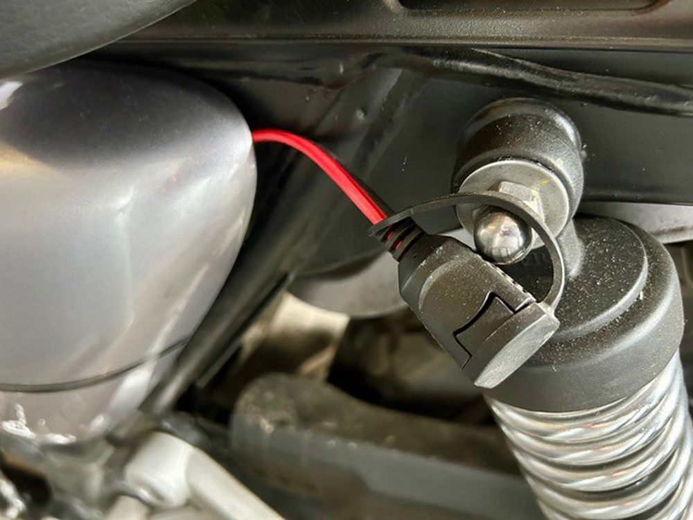 Nahaufnahme eines roten Kabels, das an einen schwarzen Schalter an der Federung eines Motorrads angeschlossen ist.