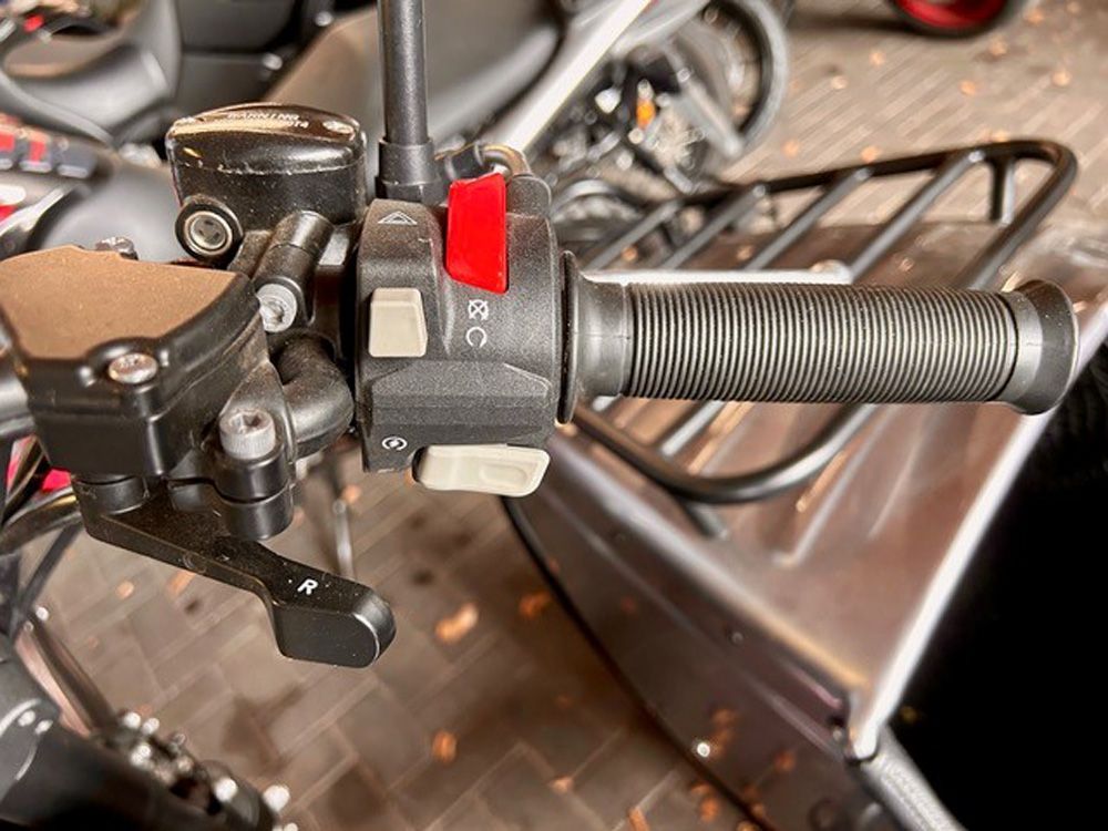 Nahaufnahme eines Gasgriffs und Bedienelementen am Motorradlenker mit rotem Knopf und schwarzem Griff.