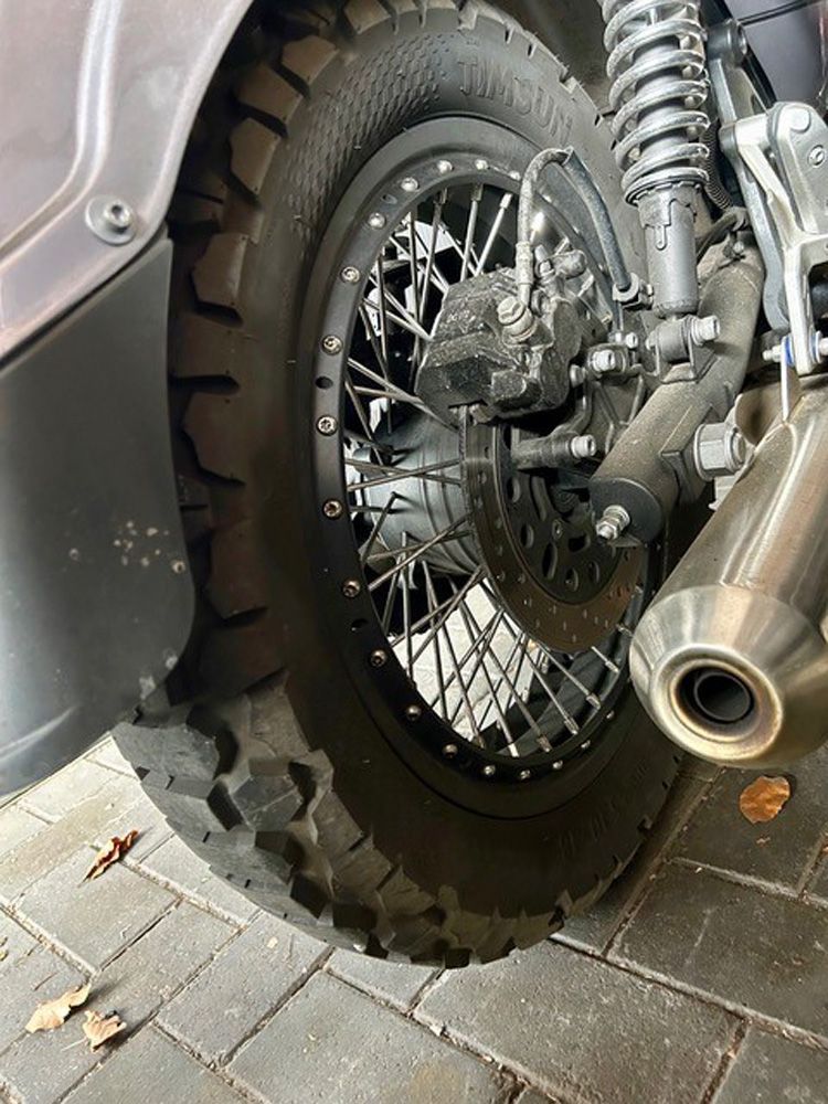 Nahaufnahme eines Motorradhinterrads, der Kette und des Auspuffs auf einem Ziegelpflaster.