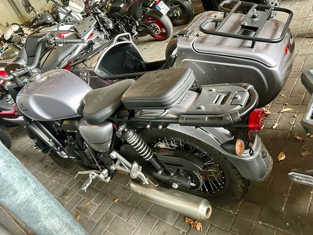 Ein schwarzes Cruiser-Motorrad parkt zwischen anderen Motorrädern auf einem gepflasterten Gehweg.