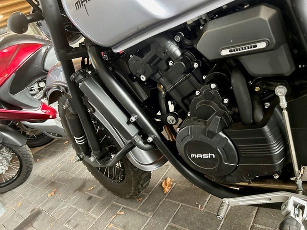 Nahaufnahme eines schwarzen Motorradmotors und der Seitenverkleidung; im Hintergrund ist ein rotes Motorrad zu sehen.