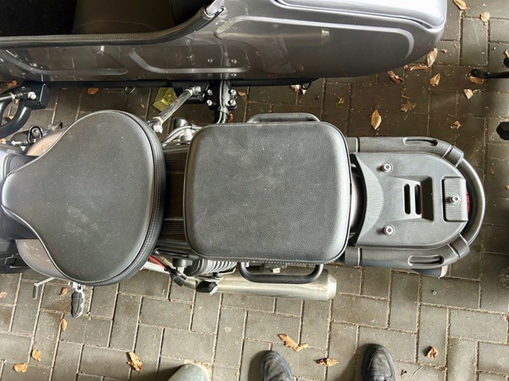 Draufsicht auf ein schwarzes Motorrad, das auf einem mit Laub bedeckten Backsteinpflasterweg geparkt ist.