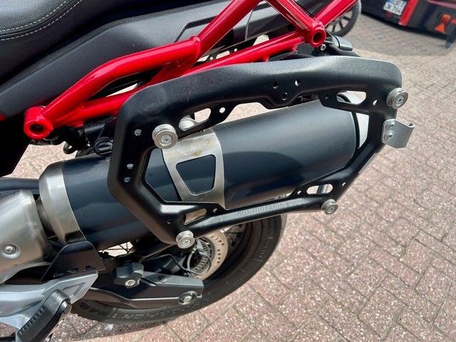 Nahaufnahme eines Motorradauspuffs mit schwarzem Hitzeschild und rotem Rahmen, geparkt auf dem Bürgersteig