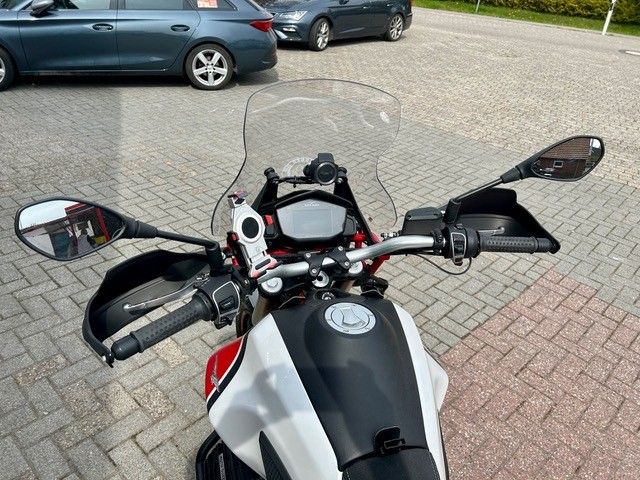 Motorradlenkeransicht, geparkt auf einem gepflasterten Parkplatz, im Hintergrund Autos.