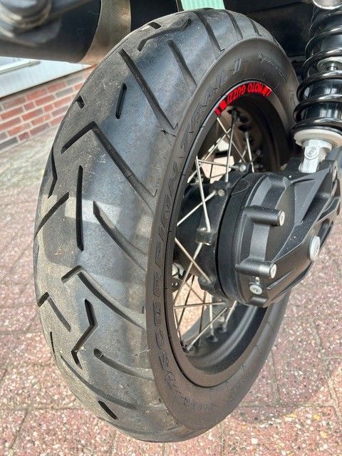 Nahaufnahme eines Motorradvorderrads mit schwarzem Reifen und silbernen Speichen auf dem Asphalt.