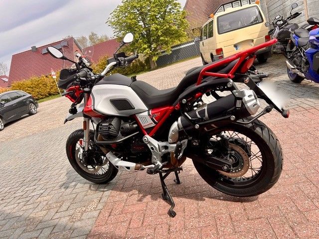 Ein weiß-rotes Motorrad parkt auf einer gepflasterten Auffahrt; im Hintergrund sind Häuser und andere Fahrzeuge zu sehen.