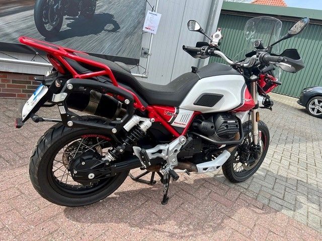 Ein rot-weißes Motorrad parkt auf dem Bürgersteig vor einem Glasgebäude.