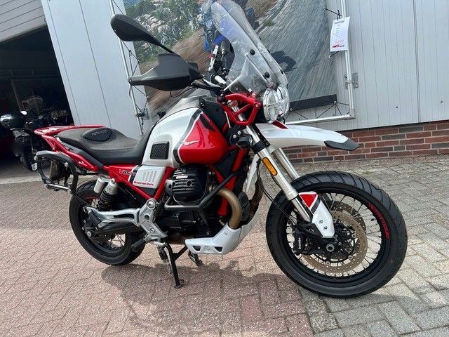 Ein rot-weißes Adventure-Motorrad parkt auf einer gepflasterten Auffahrt neben einer Garage.