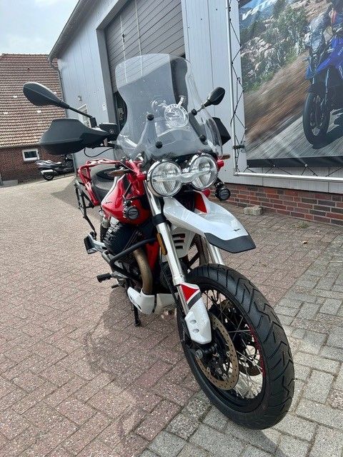 Ein weiß-rotes Adventure-Motorrad parkt vor einem Gebäude auf einem gepflasterten Parkplatz.