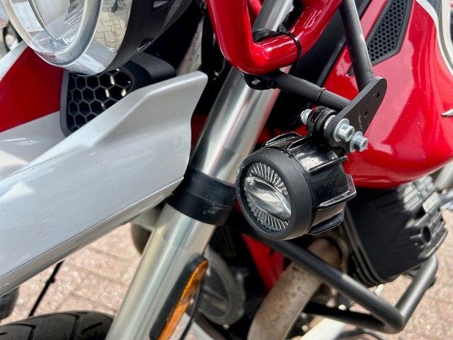 Nahaufnahme der Vorderradgabel, des Scheinwerfers und des Motorraums eines roten Motorrads mit angebrachtem schwarzem Zubehörteil.