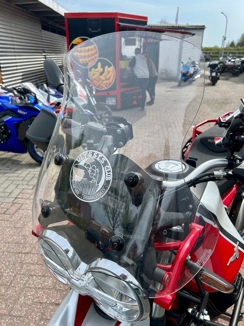 Ein Motorrad mit durchsichtiger Windschutzscheibe parkt zwischen anderen Motorrädern vor einem Geschäft.