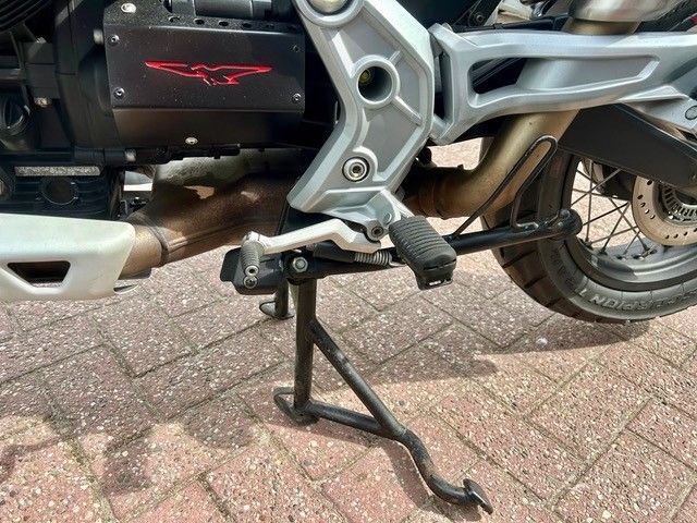 Motorrad auf dem Hauptständer, Hinterrad und silberner Rahmen auf dem Backsteinpflaster zu sehen.