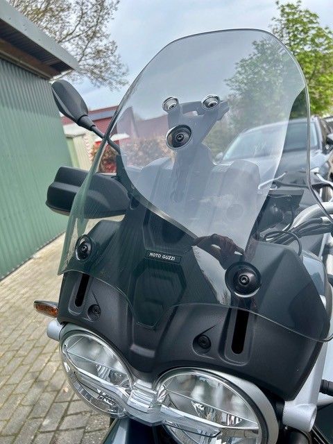 Motorrad mit klarer Windschutzscheibe und Doppelscheinwerfern parkt im Freien neben einem grünen Gebäude