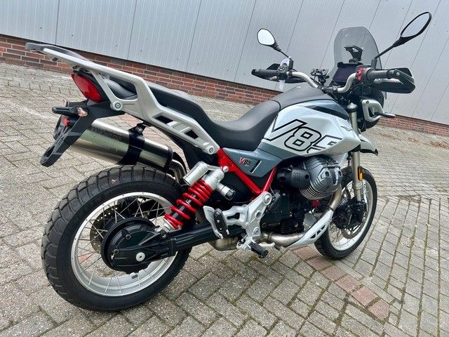 Silbernes und schwarzes Motorrad, geparkt auf einem Backsteinpflaster, Seitenansicht mit roten Hinterradfedern und Windschutzscheibe.