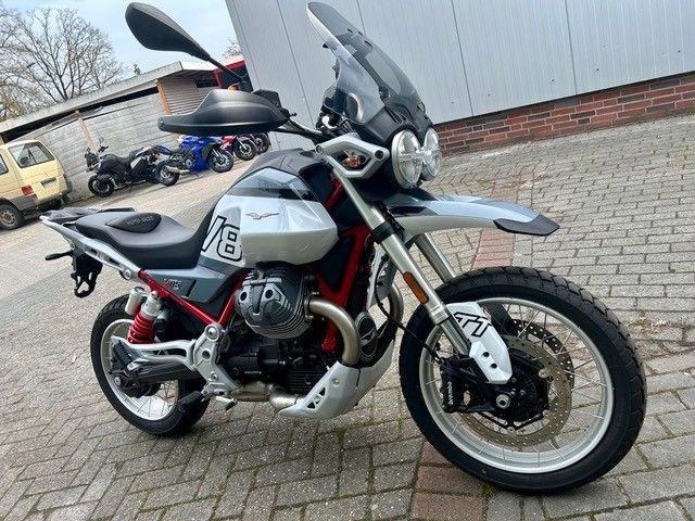 Silbernes Adventure-Motorrad, geparkt auf einem gepflasterten Gehweg, Frontansicht mit Windschutzscheibe und Topcase.