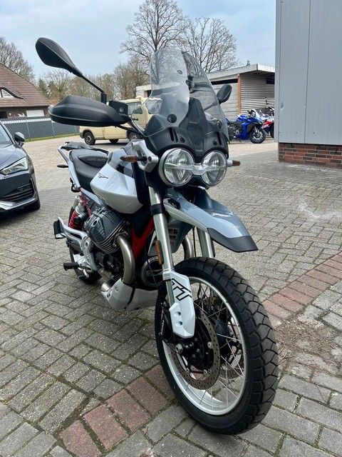 Weißes Adventure-Motorrad mit Windschutzscheibe und Seitenkoffern parkt auf einer gepflasterten Auffahrt im Freien