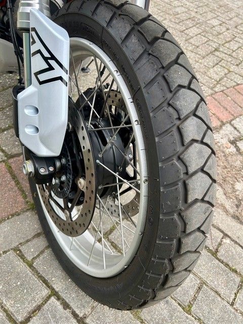 Nahaufnahme eines Motorradvorderrads mit Speichenfelge und Scheibenbremse auf Ziegelpflaster