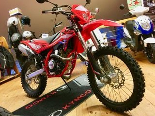Ein rotes Dirtbike steht auf einer Matte mit der Aufschrift „Kymco“