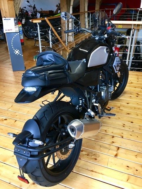 Ein schwarzes Motorrad steht auf einem Holzboden in einem Ausstellungsraum.