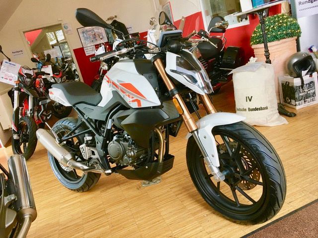 Ein Motorrad steht auf einem Holzboden in einem Ausstellungsraum.