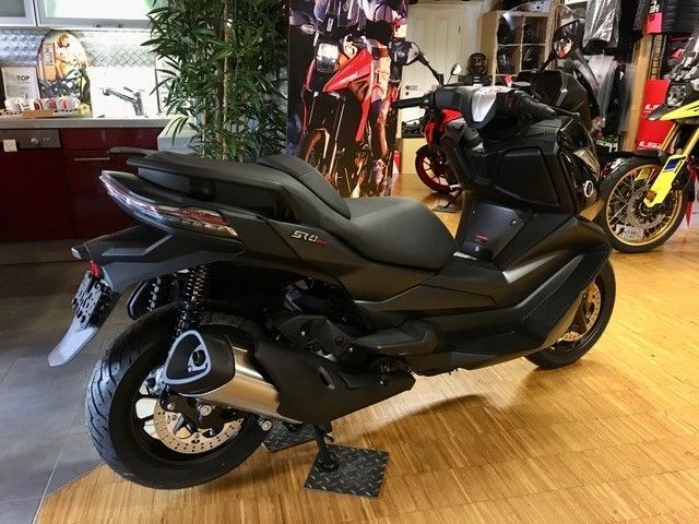 Ein schwarzer Motorroller steht auf einem Holzboden in einem Ausstellungsraum.