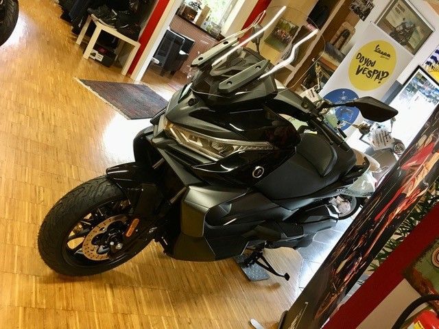 Ein schwarzes Motorrad ist in einem Raum mit einem gelben Schild mit der Aufschrift Vespa geparkt