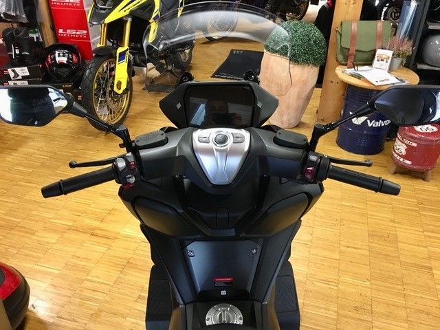 Ein schwarzer Roller ist in einem Raum mit anderen Motorrädern geparkt