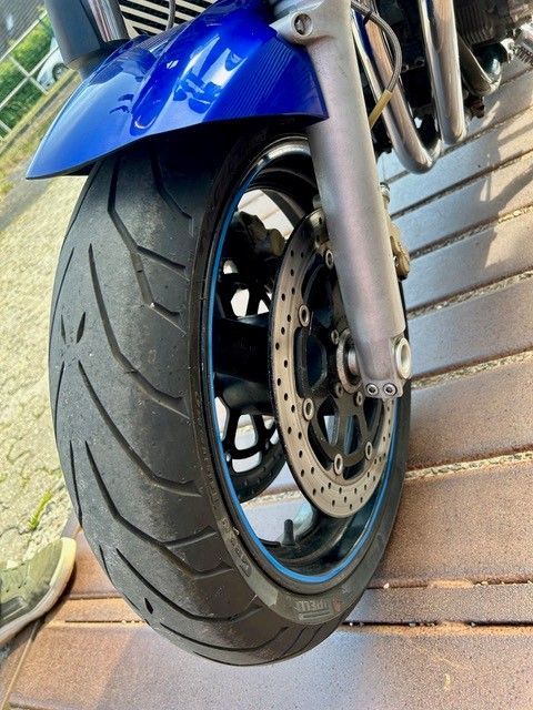 Nahaufnahme eines blauen Motorradvorderrads und der Bremse auf einer gefliesten Oberfläche
