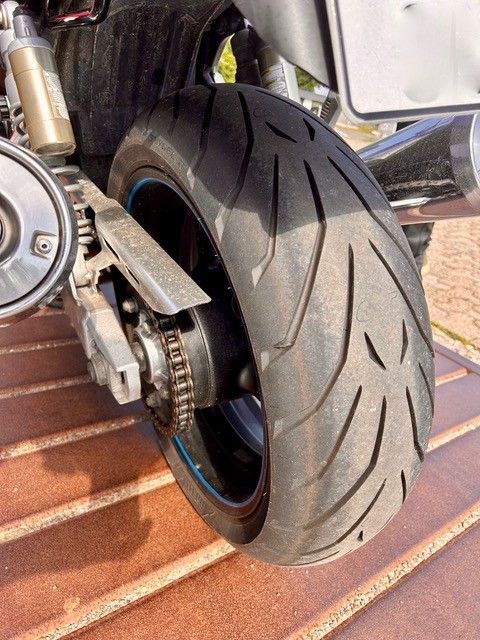 Nahaufnahme eines Motorradhinterrades mit breitem schwarzen Reifen auf einem Ziegelpflaster.