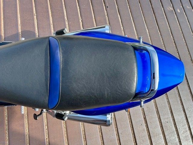 Draufsicht auf ein blau-schwarzes Motorrad, das auf einer Holzterrasse geparkt ist.