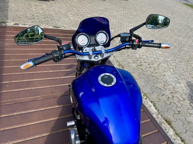 Blaues Motorrad, geparkt auf einer gepflasterten Fläche, von oben betrachtet, Spiegel und Lenker sind sichtbar.