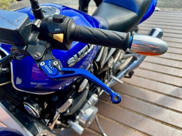 Nahaufnahme eines blauen Suzuki-Motorradlenkers und -Tanks auf einer Holzterrasse.