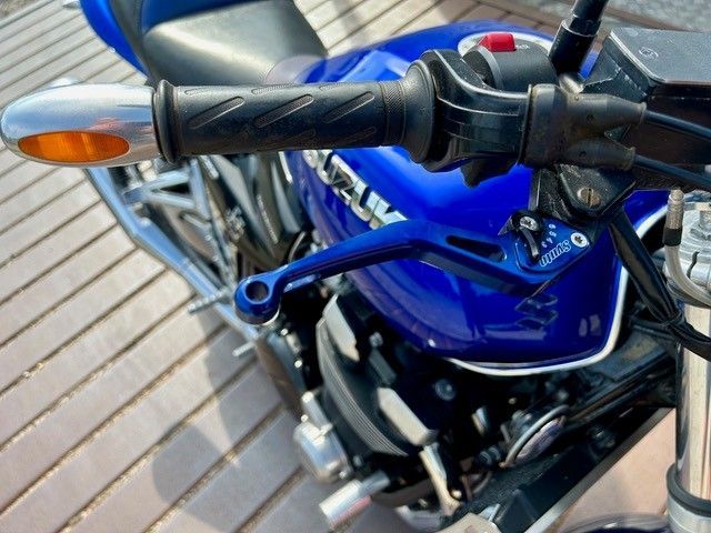 Nahaufnahme eines blauen Motorradlenkers und der vorderen Verkleidung mit Blinker, das im Freien geparkt ist.