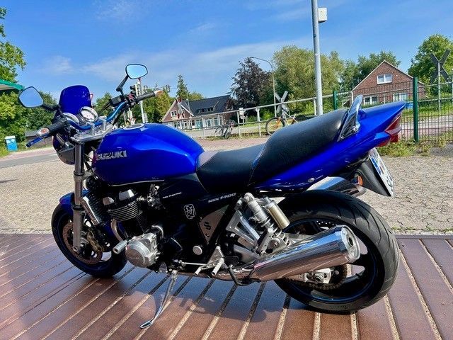 Ein blaues Sportmotorrad parkt tagsüber auf einem gepflasterten Gehweg in der Nähe einer Straße und von Häusern.