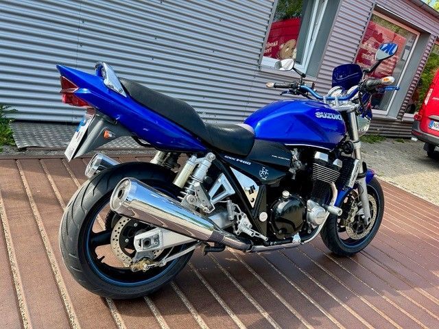 Ein blaues Sportmotorrad parkt auf einer Holzterrasse neben einem Gebäude mit Metallverkleidung.