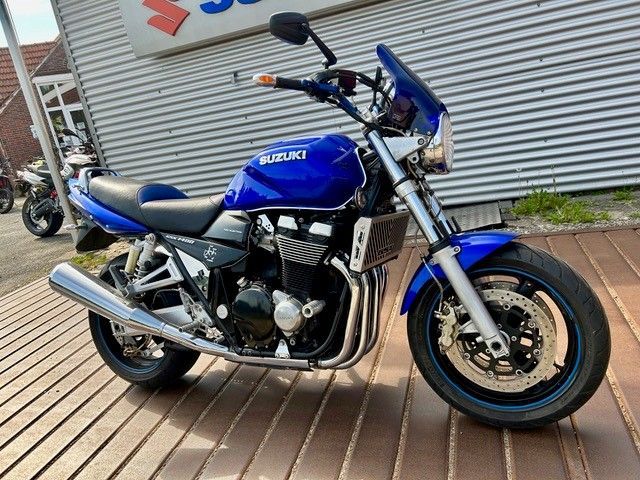 Ein blaues Suzuki-Motorrad steht auf einer Holzterrasse neben einer Wellblechwand.