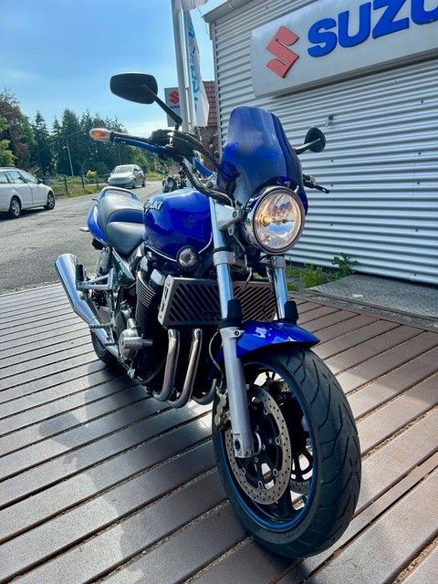 Ein blaues Suzuki-Motorrad parkt vor einem Autohaus auf einer Holzterrasse.