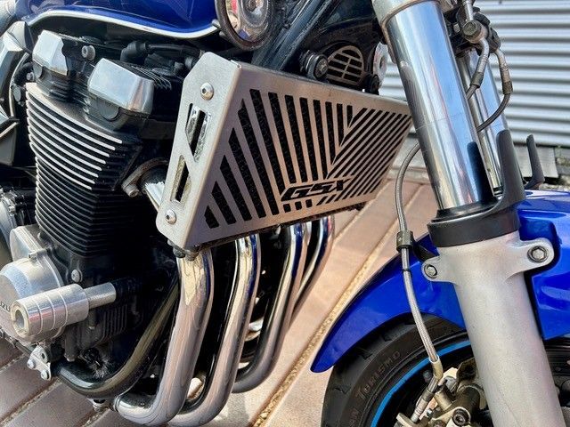 Nahaufnahme eines blauen Motorradmotors mit verchromten Auspuffrohren und einer belüfteten Seitenabdeckung