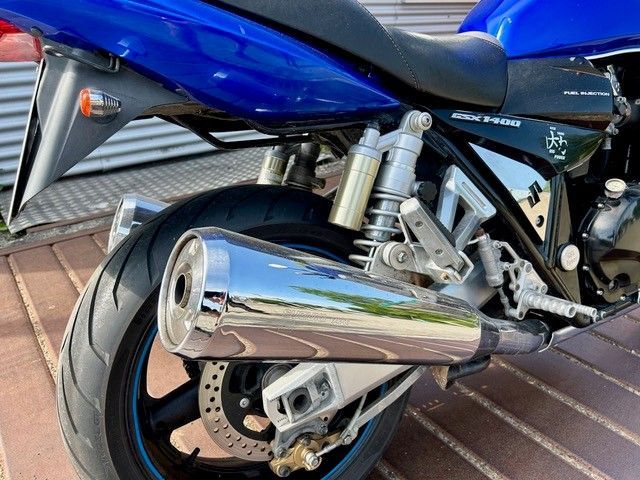 Nahaufnahme des verchromten Auspuffs und Hinterrads eines blauen Motorrads auf einem Backsteinbürgersteig