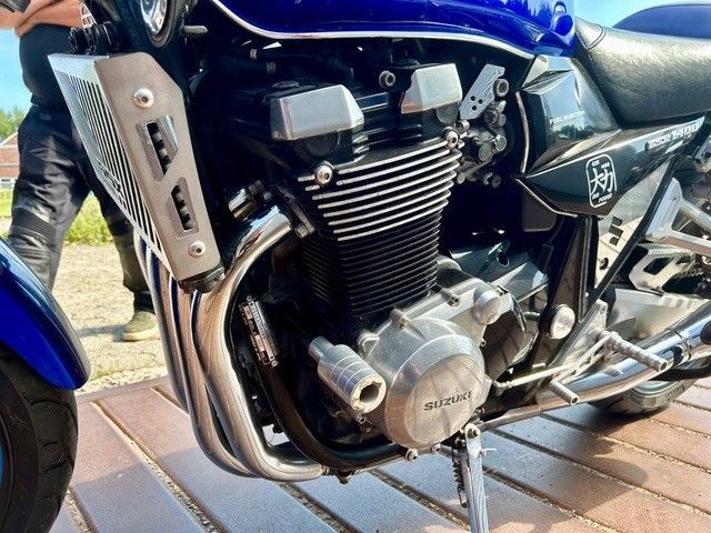 Nahaufnahme eines blauen Motorradmotors und eines verchromten Auspuffs auf einem Holzdeck