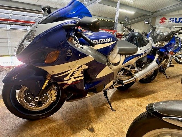Blaue und silberne Suzuki-Motorräder parken in einem Autohaus oder Ausstellungsraum.