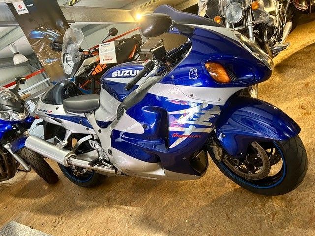 Ein blaues Suzuki-Sportmotorrad ist in einem Innenraum zwischen anderen Motorrädern ausgestellt.