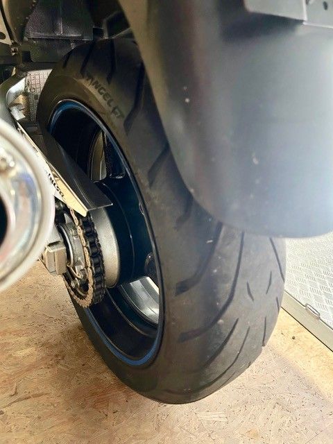 Nahaufnahme eines Motorradhinterrades mit schwarzem Reifen und silberner Felge in einer Garage.