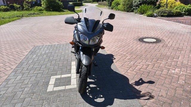 Schwarzes Motorrad, geparkt auf einem mit Ziegeln gepflasterten Platz im hellen Sonnenlicht, von vorne betrachtet.